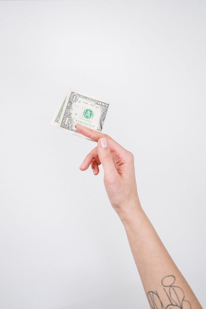 Close-up of a tattooed hand holding a US dollar bill against a plain background.